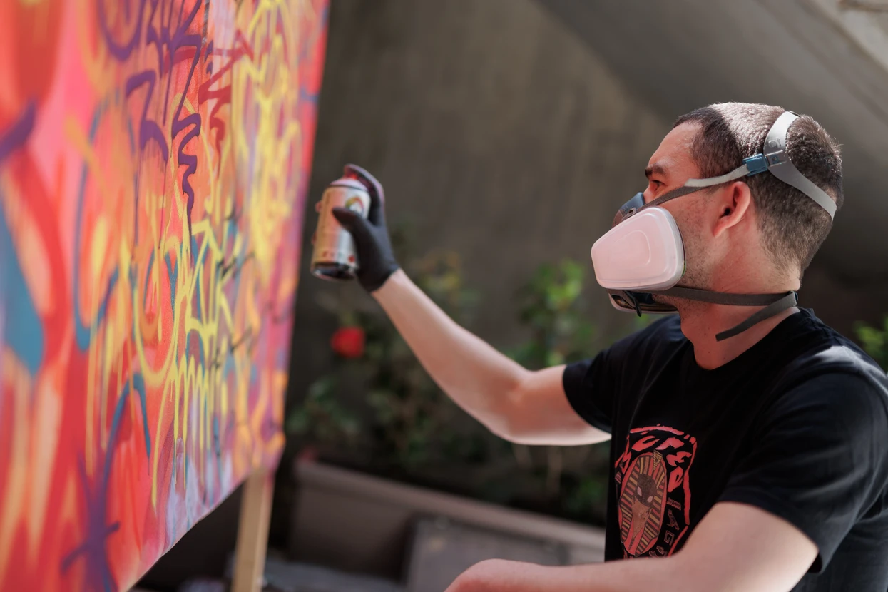 Photographie d'une fresque murale colorée et détaillée peinte sur un mur urbain, représentant un artwork de street art professionnel avec des lignes graphiques nettes, des couleurs vibrantes et harmonieuses, montrant clairement le travail d'un artiste qualifié. Le mur, situé sur une façade ou dans un contexte urbain, doit être intact et en bon état, sans traces de dégradation, mettant en avant le résultat fini d'une réalisation de qualité professionnelle.